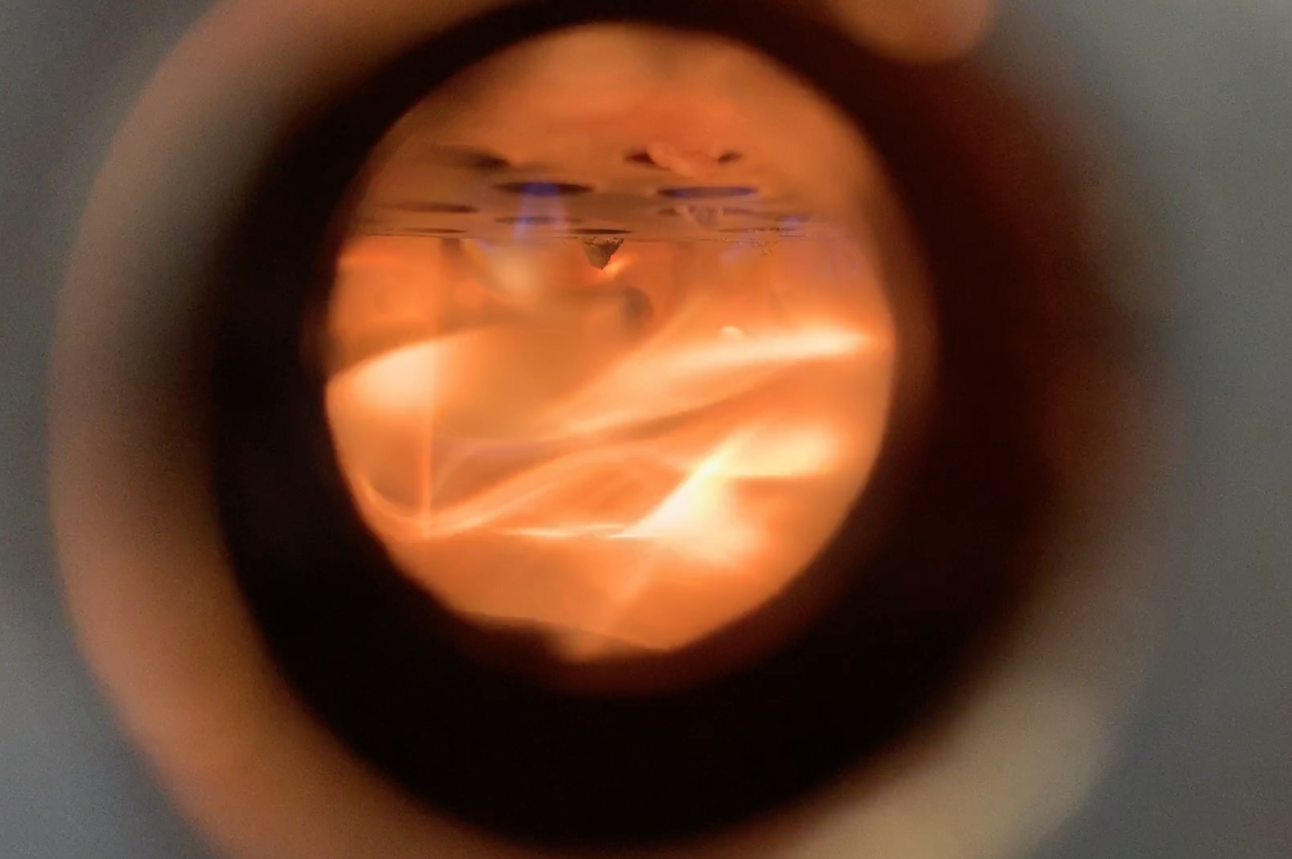 We have developed a combustion chamber for the incinerator that creates a downward flowing air draft, resulting in flames burning from the bottom of the fuel rather than the top.