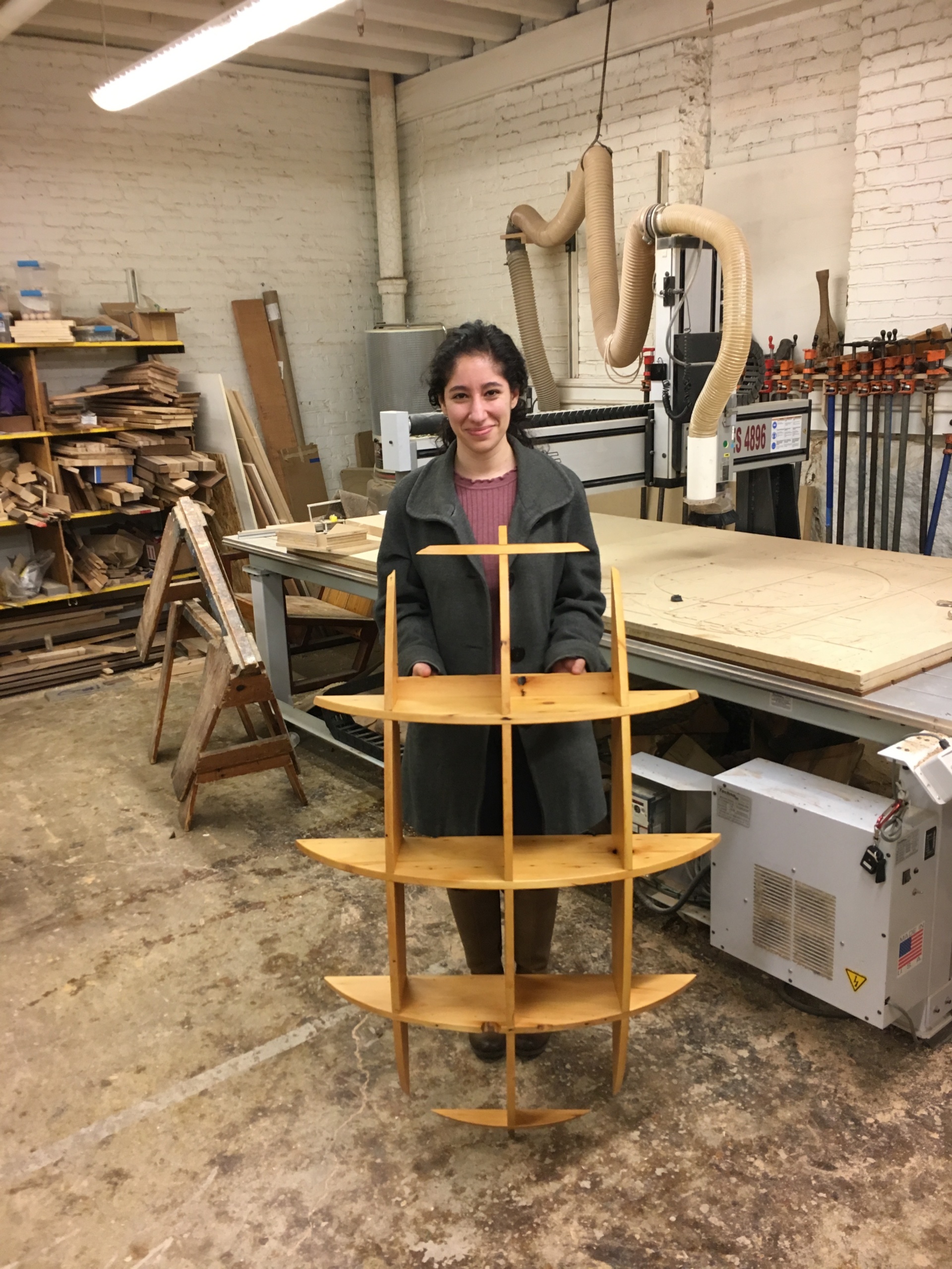 Michal learned wood working in the Hobby Shop and has become one of our most skilled members. Here, she is holding a recently completed set of shelves made from reclaimed old growth pine.